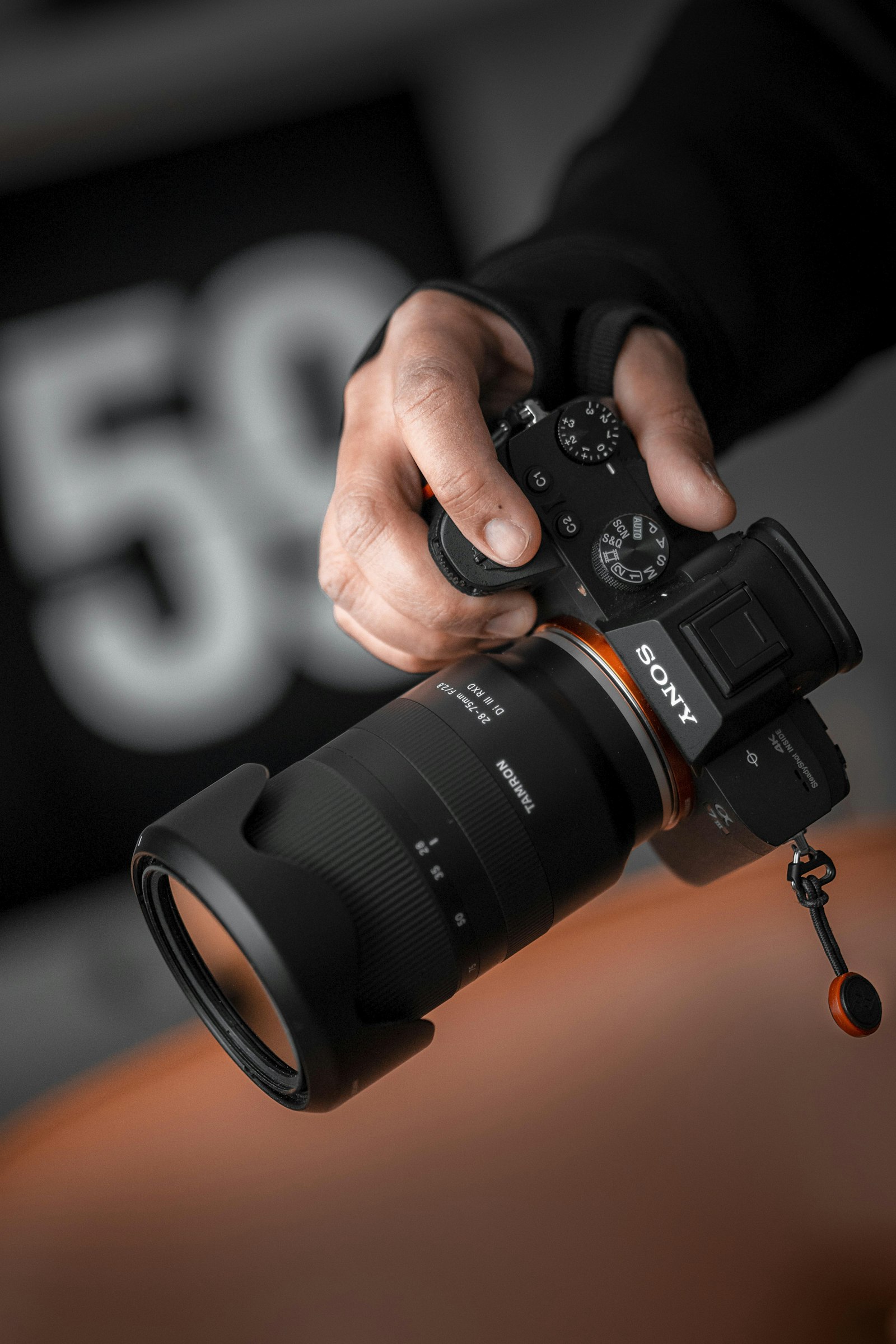 Fotograf cu Sony Alpha și obiectiv 28–75mm Tamron pe fundal orange